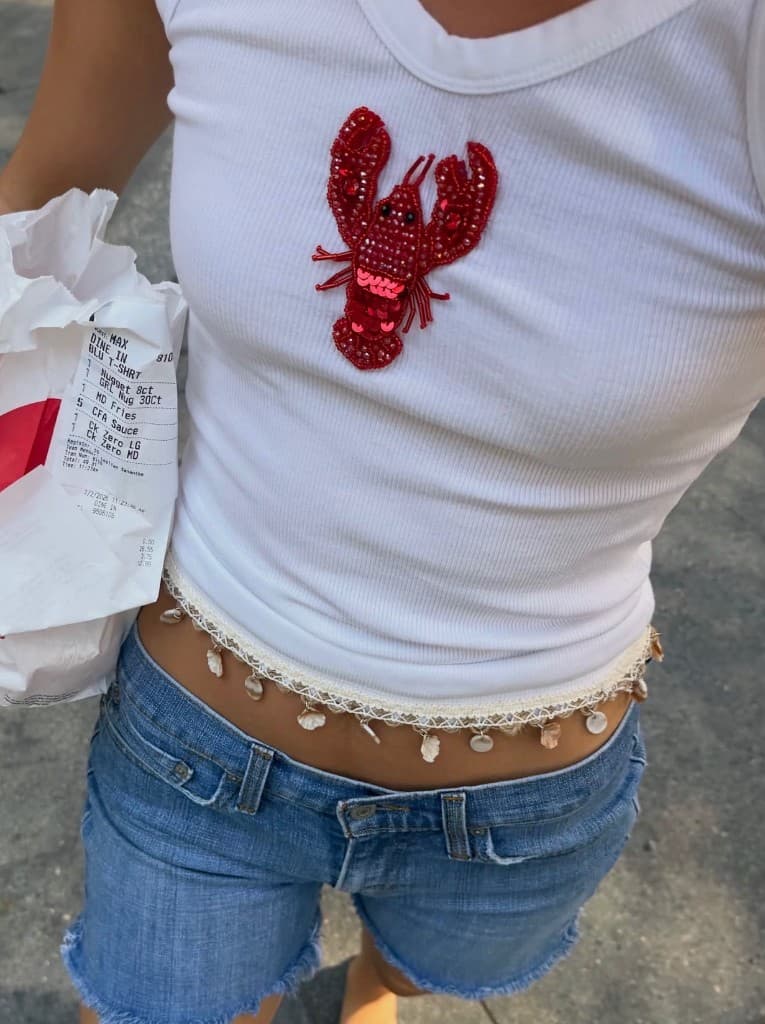 White ribbed tee with a beaded lobster patch, denim shorts, and seashell waist trim