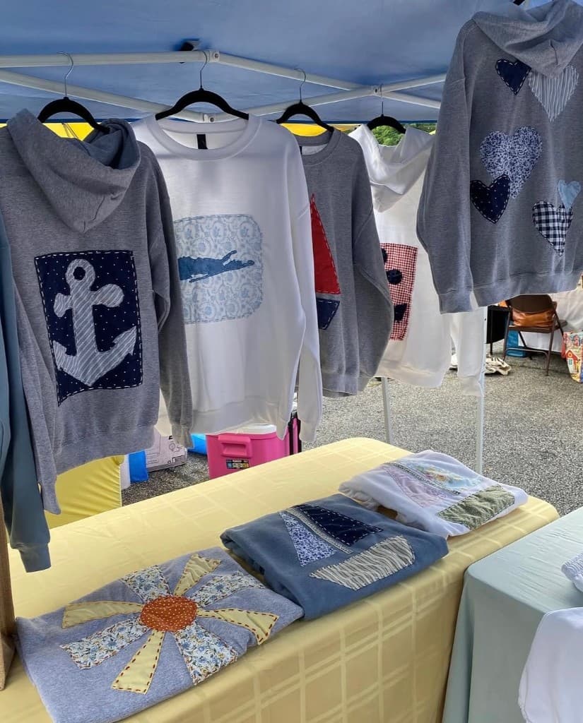 Coast Collection booth with appliqué sweatshirts hanging under a blue market tent